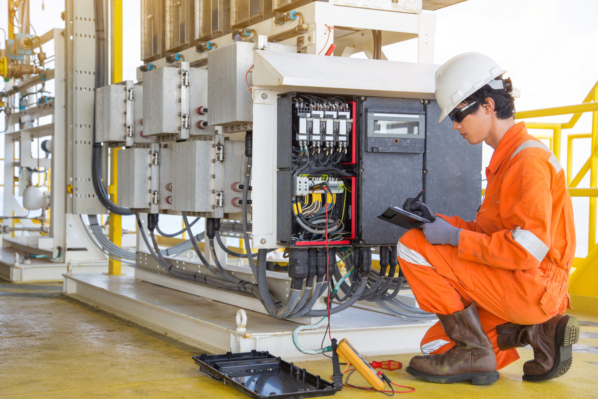 Electrical and instrument technician measuring voltage of thermo electric generator and record reading value to maintenance sheet for annual inspection at offshore oil and gas remote platform.
